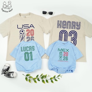 May include: A collection of children's apparel, including two beige t-shirts and two light blue onesies. The t-shirts feature "USA 2026" and "HENRY 03" graphics. The onesies display "LUCAS 01" and "MEX 2026" designs. Sunglasses and baby shoes are also visible.