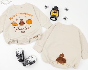 May include: Beige baby bodysuit with long sleeves, featuring a Thanksgiving design with a turkey, pumpkin, and the text "My First Thanksgiving" and "Amelia 2025". Includes a pair of black and white sneakers.
