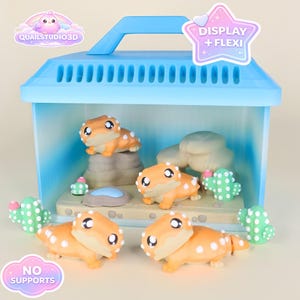 May include: A light blue terrarium-style display case with a handle, housing four orange and white spotted lizard figurines, along with cacti and rock formations. The case has the text "DISPLAY + FLEXI" and "NO SUPPORTS".
