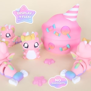 May include: A collection of pink dragon figurines and a cupcake-shaped container. The figurines have large eyes and colorful wings. The container is decorated with candy-shaped embellishments and a striped cone. The image includes text that says "DISPLAY + FLEXI" and "NO SUPPORTS".