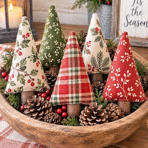Peut inclure: Cinq sapins de Noël en tissu en forme de cône dans un bol en bois avec des pommes de pin et des baies rouges. Les arbres présentent divers motifs, dont un tartan rouge et vert, un fond crème avec du houx, du vert uni avec des brindilles et du rouge.