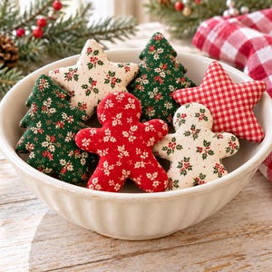 May include: A white ceramic bowl filled with fabric ornaments in the shapes of stars, Christmas trees, and gingerbread people. The ornaments feature patterns of red and green holly leaves, red and white gingham checks, and solid red fabric.