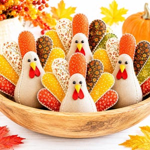 May include: Three stuffed fabric turkey figures with beige bodies, yellow beaks, and red wattles. Each turkey has a fan-shaped tail made of multiple fabric petals in various autumn colors and patterns, including orange, yellow, brown, and floral prints.