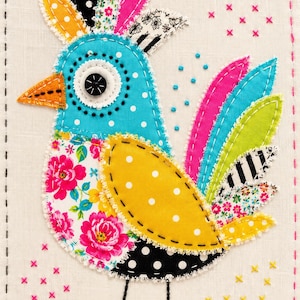 May include: A textile art piece featuring a bird made of various fabric patches. The bird has a blue polka-dot head, a floral chest, a yellow polka-dot wing, and a multi-coloured tail. It features a black button eye, an orange beak, and black embroidered legs on a cream background with pink and yellow cross-stitch accents.