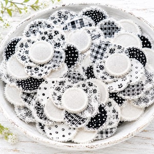 May include: A collection of circular fabric facial pads in a white bowl. The pads feature various black and white patterns including floral prints, polka dots, and gingham checks, with some solid white textured fabric sides and frayed edges.