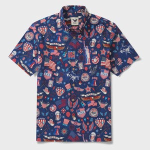 Puede incluir: Camisa de manga corta azul marino con un estampado repetido de símbolos patrióticos estadounidenses. El diseño incluye banderas, la Estatua de la Libertad, estrellas y jarras de cerveza en rojo, blanco y azul.