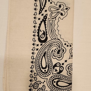 May include: An off-white bandana featuring a black paisley print pattern. The fabric is folded into a rectangular shape. The text "Off-White" is printed in yellow at the top of the image, positioned above the patterned textile accessory.