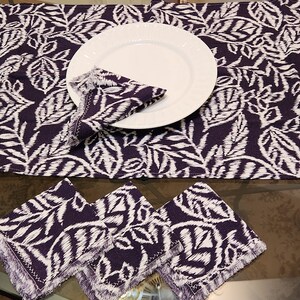 May include: A set of purple and white table linens with a leaf pattern. The set includes a table runner and four placemats.