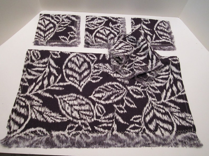 May include: Set of five purple and white patterned fabric placemats with fringed edges. The placemats feature a leaf design.