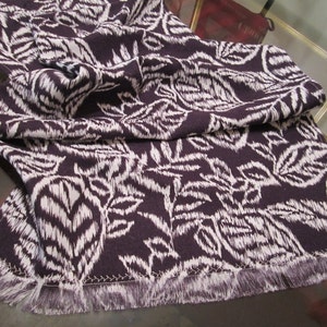 May include: A white and purple patterned table runner with a fringed edge.