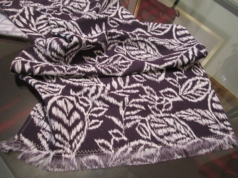 May include: A white and purple patterned table runner with a fringed edge.