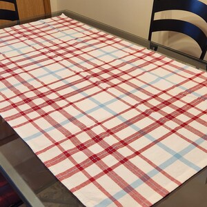 K&ouml;nnte beinhalten: Eine rot-blaue karierter Tischdecke auf einer Glastischplatte. Die Tischdecke ist wei&szlig; mit roten und blauen Streifen.