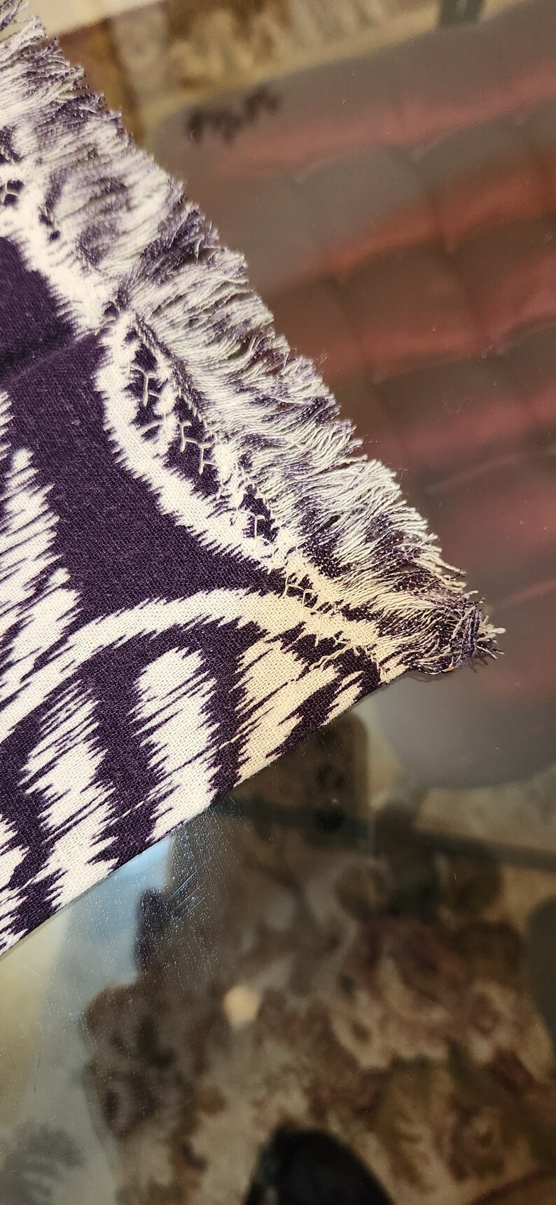 May include: A close-up of a purple and white patterned fabric with a fringed edge. The fabric has a subtle ikat design.