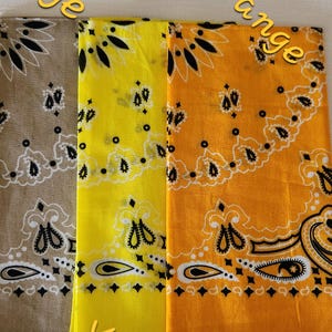 May include: Three square bandanas featuring a traditional paisley pattern in black and white. The fabric colors are beige, bright yellow, and light orange. The text Beige, Yellow, and Lt Orange is printed over each respective fabric section.