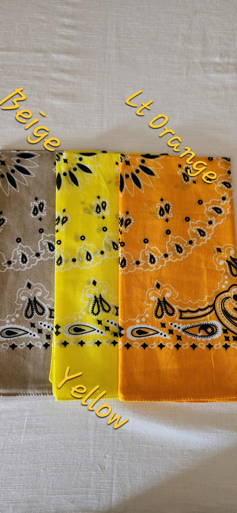 May include: Three square bandanas featuring a traditional paisley pattern in black and white. The fabric colors are beige, bright yellow, and light orange. The text Beige, Yellow, and Lt Orange is printed over each respective fabric section.