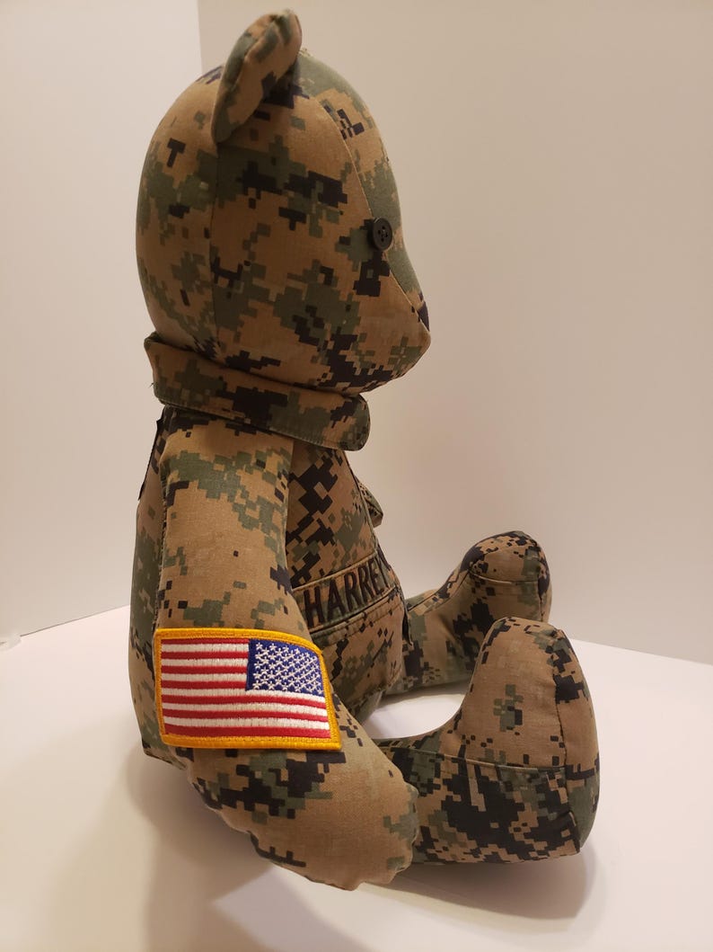 Op de afbeelding: Een teddybeer gemaakt van camouflage stof. De beer heeft een zwart knoopoog en een kleine Amerikaanse vlag patch op zijn arm. De naam "HARREN" is op de borst van de beer geborduurd.