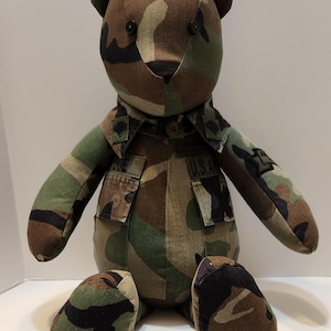 May include: Camouflage teddy bear wearing a military uniform with the text "U.S.A." on the jacket.