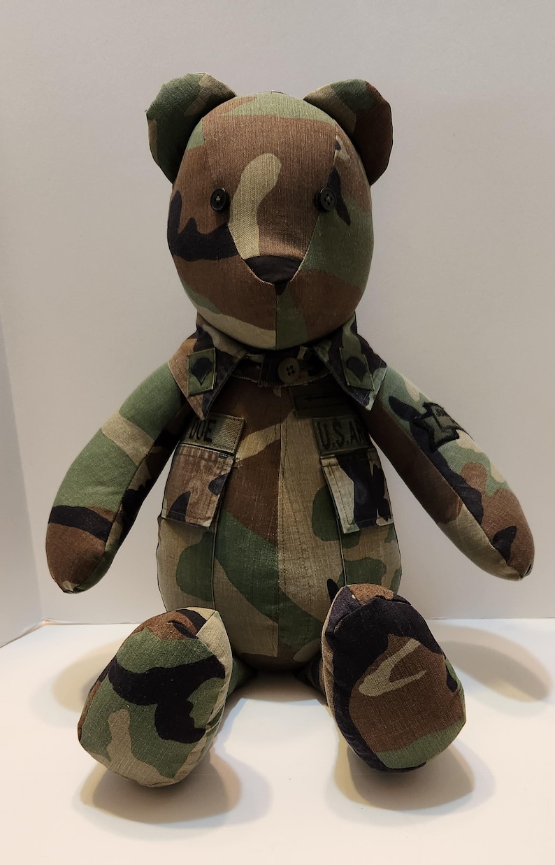 May include: Camouflage teddy bear wearing a military uniform with the text "U.S.A." on the jacket.
