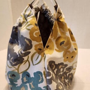 May include: A floral print tote bag with clear acrylic handles. The fabric features a pattern of yellow, blue, and gray flowers on a white background. The interior is a dark brown color.