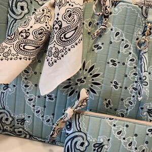 May include: A quilted tote bag, a matching zippered pouch, and a small rectangular case in a light sage green fabric featuring a black and white paisley bandana print. A white bandana with a black paisley pattern is tied to the tote handle.