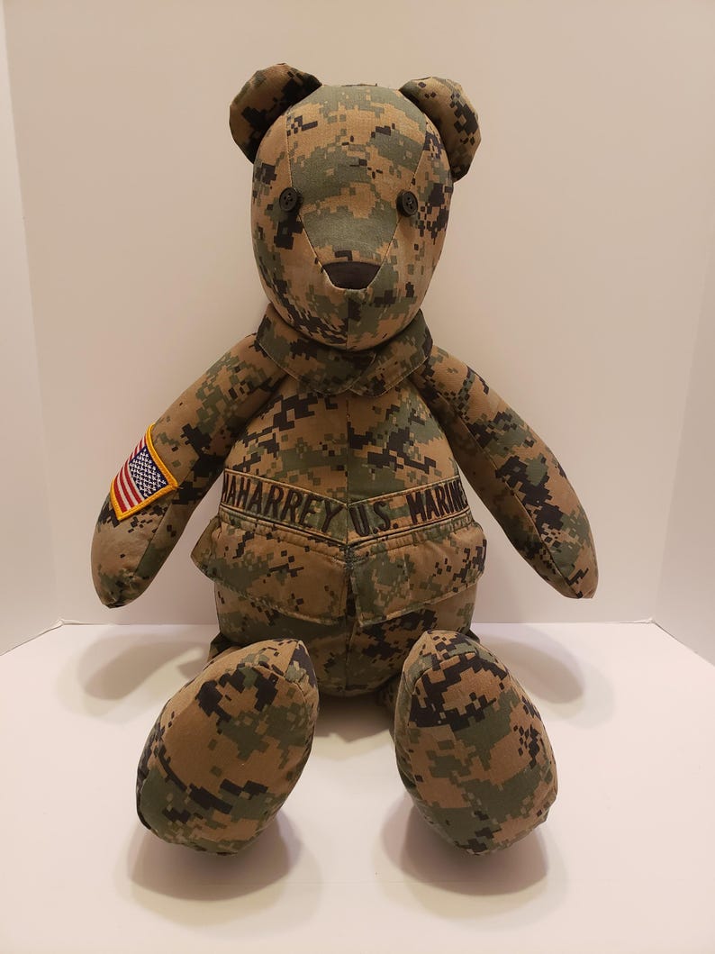 Op de afbeelding: Een handgemaakte teddybeer in een camouflagepatroon. De beer heeft knoopogen en een gestikte neus. Hij draagt een uniform met een Amerikaanse vlagpatch en de tekst "AHARREY U.S. MARINE".
