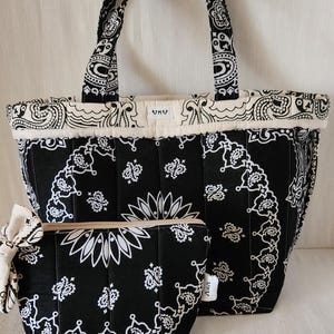 May include: A black and white quilted tote bag, a matching zippered pouch with a side bow, and a wristlet strap. Each item features a repeating paisley bandana pattern. The tote and pouch have a small white label with the text UKU.