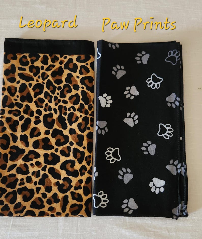 May include: Two rectangular fabric pieces displayed side by side. The left piece features a brown and black leopard print pattern with a solid black top border. The right piece is black with a repeating pattern of grey and white paw prints.