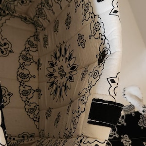 May include: A quilted fabric basket featuring a black and white paisley bandana print. The interior and exterior are lined with the same patterned textile, and the rim includes black fabric tabs. The structure is soft, flexible, and cylindrical.