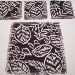 May include: Set of four black and white fabric coasters with a fringed edge. The coasters feature a floral pattern.