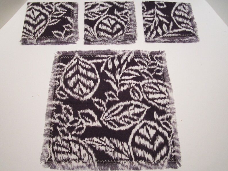 May include: Set of four black and white fabric coasters with a fringed edge. The coasters feature a floral pattern.