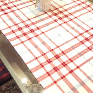 K&ouml;nnte beinhalten: Eine wei&szlig;e Tischdecke mit rotem und blauem Karomuster auf einem Glastisch mit einer Topfpflanze in der Mitte.