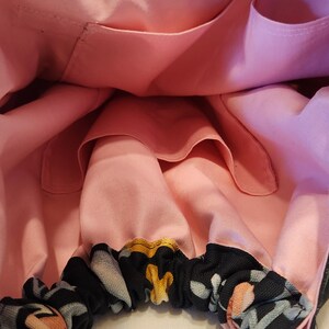 May include: A handmade tote bag with a black floral pattern on the exterior and a light pink interior. The bag has a black handle and several interior pockets. The floral pattern includes yellow, gray, and peach-colored flowers.