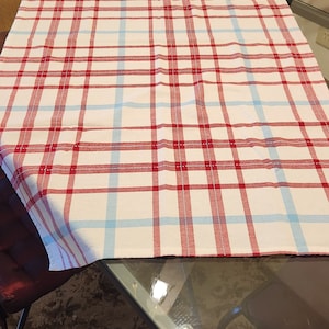 K&ouml;nnte beinhalten: Eine rot-blaue karierte Tischdecke auf einem Glastisch mit zwei schwarzen St&uuml;hlen. Die Tischdecke ist in der Mitte gefaltet.
