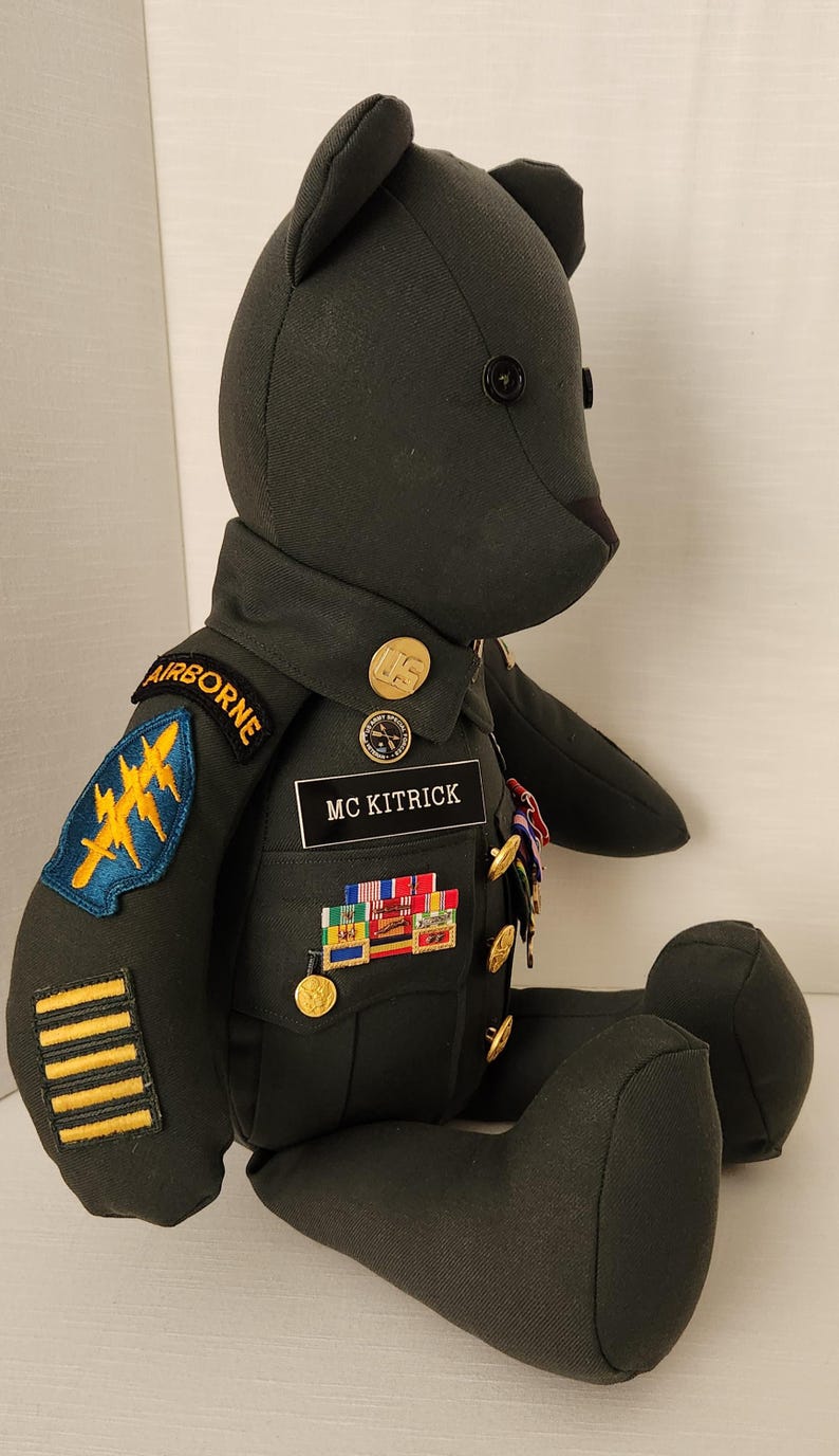Op de afbeelding: Een donkergroene teddybeer met een militair uniform. Het uniform heeft patches met "AIRBORNE" en "MC KITRICK". De beer heeft gouden knopen en diverse medailles.