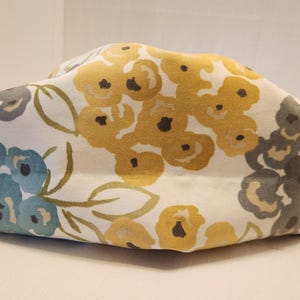 May include: A rectangular fabric container with a floral pattern. The design features yellow, blue, and gray flowers on a white background. The container is likely used for storage or as a decorative item.
