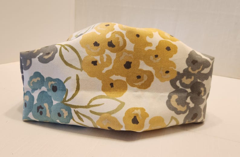 May include: A rectangular fabric container with a floral pattern. The design features yellow, blue, and gray flowers on a white background. The container is likely used for storage or as a decorative item.