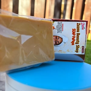 May include: A wrapped bar of soap and a box from Zazou Beauty Shop. The soap is a light orange colour and is in a clear plastic wrapper. The box has the words "Zazou Beauty Shop SOAP Papaya" printed on it.