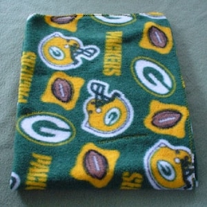 May include: Green and yellow fleece blanket with a repeating pattern of football helmets, footballs, and the Green Bay Packers logo.