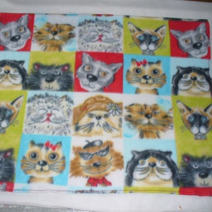 May include: A colorful fleece blanket with a patchwork design featuring various cartoon cats with different expressions. The blanket is made of soft, plush fabric and has a white background with squares of red, blue, green, and yellow.