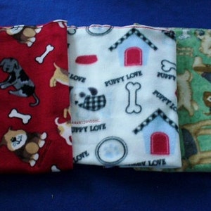 May include: Three fleece dog blankets with different puppy designs. The first blanket is red with white bones and black and white puppies. The second blanket is white with black and white checkered designs, red doghouses, and the text "Puppy Love". The third blanket is green with brown and white puppies.