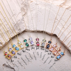 May include: A collection of cat-shaped pendant necklaces with various gemstone colors, including ruby, sapphire, and emerald. Each necklace has a delicate chain and is labeled with a month and gemstone name. The text includes "Jan" to "Dec".