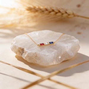 May include: A gold chain necklace featuring a horizontal bar pendant set with three rectangular baguette-cut gemstones in a row. The stones are arranged in a sequence of red, clear, and blue, creating a vibrant and colorful focal point on the chain.