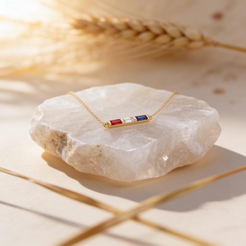 May include: A gold chain necklace featuring a horizontal bar pendant set with three rectangular baguette-cut gemstones in a row. The stones are arranged in a sequence of red, clear, and blue, creating a vibrant and colorful focal point on the chain.