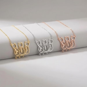 Peut inclure: Trois colliers pendentifs en forme de chat, en or, argent et or rose. Chaque collier présente trois silhouettes de chat avec des noms personnalisés : Sully, Rosie et Cactus. Les colliers sont présentés sur une surface blanche.