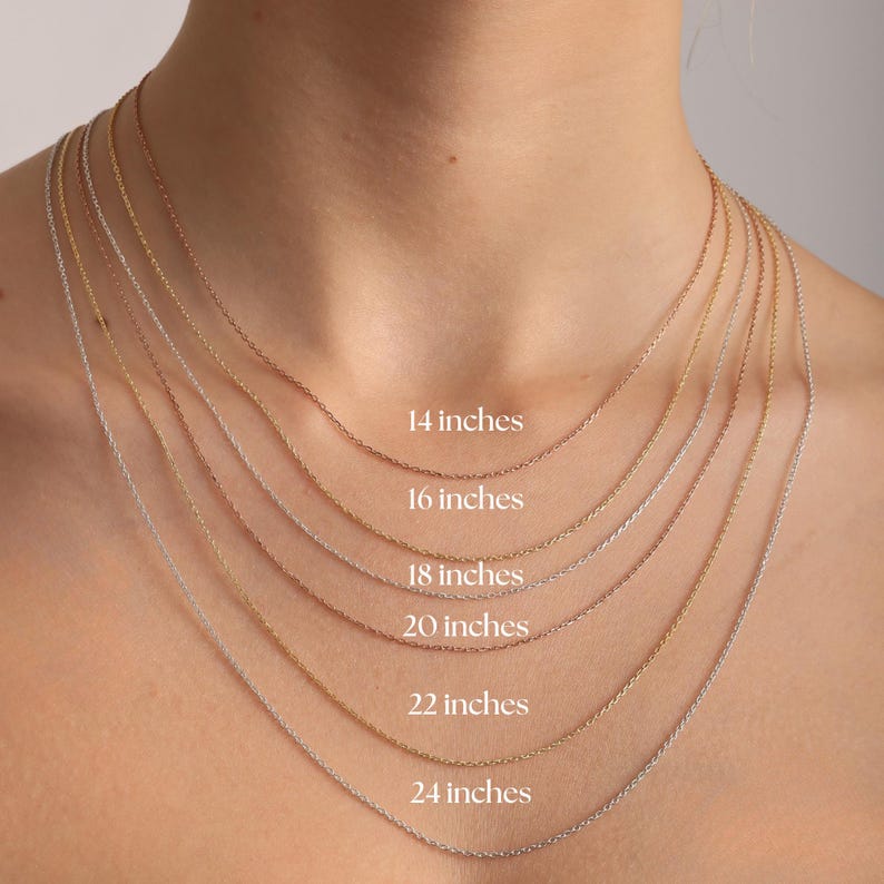 May include: A collection of six thin metal chain necklaces layered in varying lengths, labeled with text indicating sizes from 14 inches to 24 inches. The chains feature different metallic tones including silver, gold, and rose gold finishes.