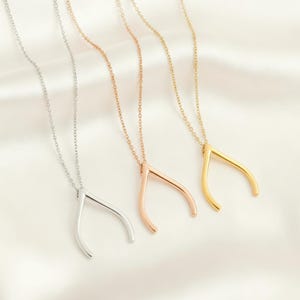 May include: Three wishbone necklaces in silver, rose gold, and gold. Each necklace features a delicate chain and a wishbone pendant. The pendants have a smooth, polished finish and are displayed on a white satin background.