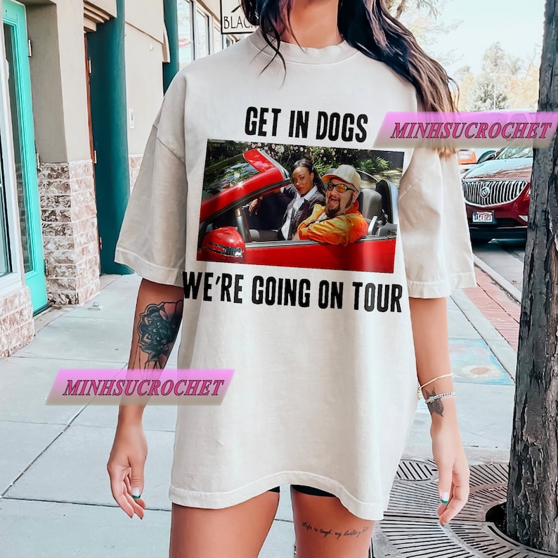 Może przedstawiać: Kremowy t-shirt z grafiką czerwonego kabrioletu z dwiema osobami. Tekst "GET IN DOGS" znajduje się nad grafiką, a "WE'RE GOING ON TOUR" poniżej. Koszulka ma luźny kr&oacute;j.