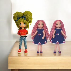 May include: Three crocheted dolls, one with green hair and a red shirt with the word "YOUTH" on it, and two with pink hair and blue dresses with white flowers.
