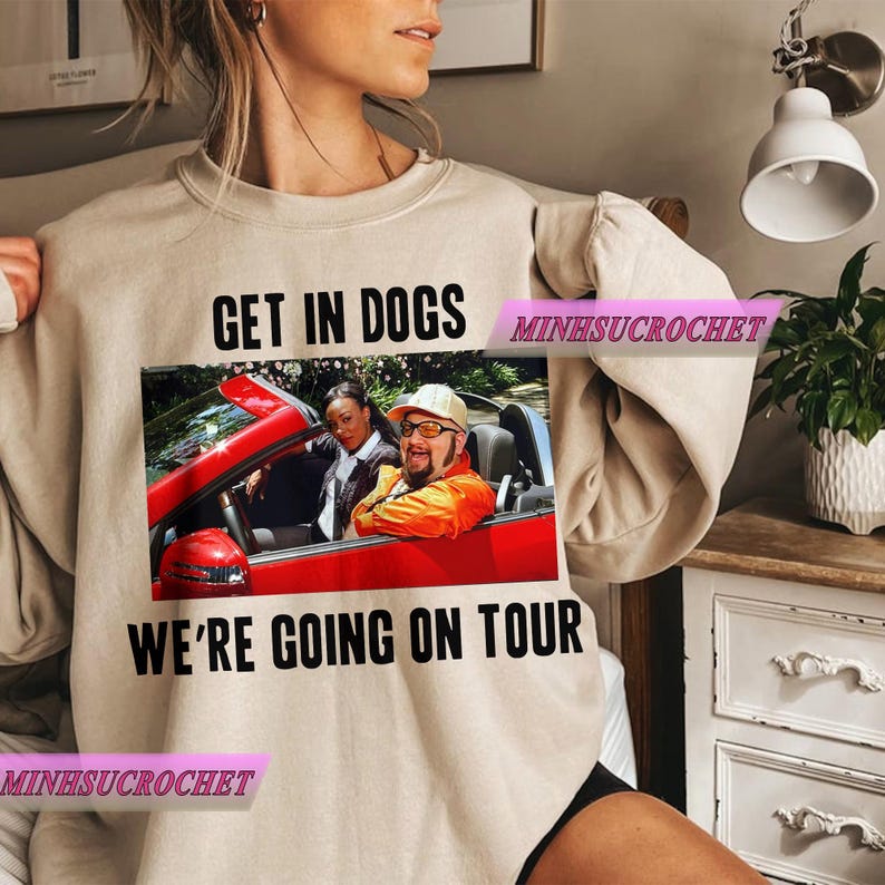 Może przedstawiać: Beżowa bluza z napisem "GET IN DOGS WE'RE GOING ON TOUR" nad i pod zdjęciem dw&oacute;ch os&oacute;b w czerwonym kabriolecie. Bluza ma długie rękawy i okrągły dekolt.