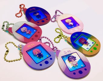 May include: Six colorful, translucent keychains shaped like a Tamagotchi, each with a different character and Korean text. The keychains are on a white background.